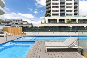 a swimming pool with a chair and a building at Executive Oceanside Apartment in Mount Maunganui