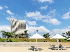 two white umbrellas and chairs with a tall building at Vias Hotel Vung Tau in Vung Tau