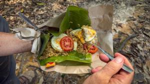 a person holding a plate of food with a fork and knife at Bukit Lawang Orangutan Dormitory in Bukit Lawang +171 photos