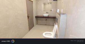 a white bathroom with a toilet and a sink at Hotel Peepal in Noida