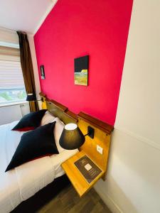 ein Schlafzimmer mit einer roten Wand, an dem ein Bett und ein Tisch stehen. in der Unterkunft Hôtel OpalOriental Boulogne Sur Mer - gare ville et centre in Boulogne-sur-Mer