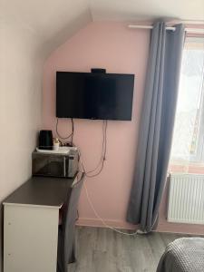 a room with a tv on a pink wall with a desk at Chambre Maria in Le Pollet