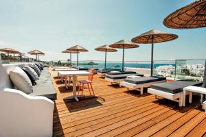 una terraza de madera con mesas, sillas y sombrillas en The George Hotel Mykonos, en Platis Gialos