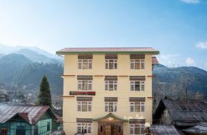 a large yellow building with windows and mountains in the background at Verdant The Vintage in Lachung
