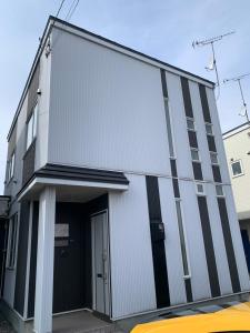 ein weißes Gebäude mit einer Tür und einem gelben Auto in der Unterkunft Bon Clair in Sunagawa