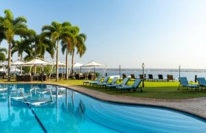 a pool with chairs and palm trees and the ocean at Hotel Cardoso in Maputo
