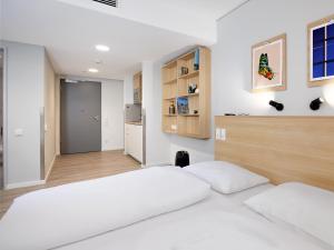 a white bedroom with two beds and a kitchen at smartments Frankfurt Airport in Frankfurt