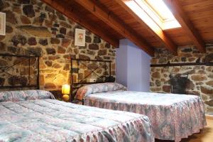 a bedroom with two beds and a stone wall at Apartamentos La Barcenilla in Herada