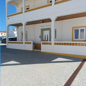 a white building with a door in a parking lot at Hostel Nature - Zambujeira do Mar in Zambujeira do Mar