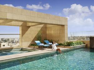 a woman sitting on the edge of a swimming pool at Fairmont Amman in Amman