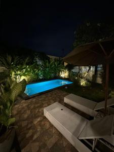 a swimming pool at night with two chairs and an umbrella at Muno House in Seminyak