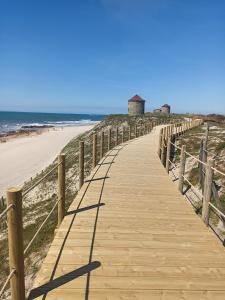 a wooden path leading to a beach with a lighthouse at Casa do Sol - Entre o Mar e o Pinhal in Apúlia
