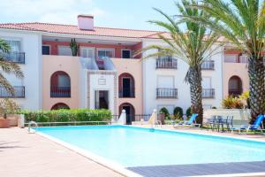 a swimming pool in front of a building with palm trees at Vila da Praia 462-C01 in Óbidos