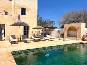 a swimming pool with chairs and an umbrella next to a house at Palais Zoa in Essaouira