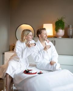 a man and woman in white robes sitting on a bed with drinks at Grand Hyatt Berlin in Berlin