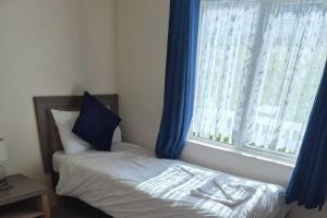 a bedroom with a bed with blue curtains and a window at 2 Bed Caravan - Sleeps 6 - Pets - Pool - Parking in Newquay