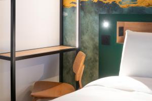 a bedroom with a bed and a chair and a wall at Kyriad Argenteuil in Argenteuil