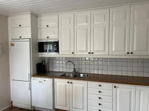 a kitchen with white cabinets and a sink and a refrigerator at Gästhus i Västanbyn, Sandviken in Sandviken