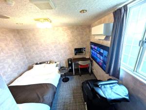 a bedroom with a bed and a television and a suitcase at セルフプラスホテル銚子無人ホテル in Choshi