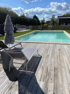 a pool with a chair and an umbrella on a wooden deck at La maison du bois brulée 5 in Villaines-les-Rochers
