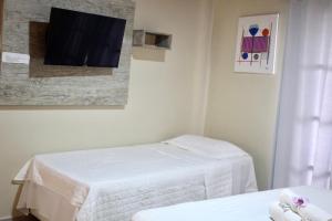 a room with two beds and a tv on the wall at Suíte Atobás in Arraial do Cabo