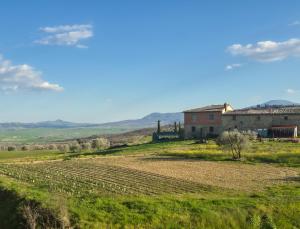 a farm with a field and a building in the background at My Tuscany Pink Suite in San Quirico dʼOrcia