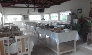a dining room with white tables and chairs and windows at Hotel Pousada Gurupiá in Serra Negra