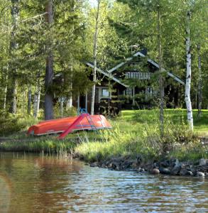 ein rotes Boot, das am Ufer eines Flusses liegt, mit einem Haus in der Unterkunft Pohja in Joensuu