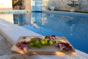 a cutting board with meat and grapes next to a swimming pool at Villa Marko in Ljubitovica