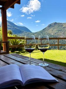 two glasses of wine and an open book on a wooden table at Casa 04 Monte Boa Vista - Conforto com Piscina Privativa, Sauna e Lareira in Teresópolis