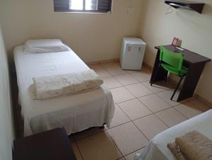 a room with two beds and a desk and a green chair at Restaurante e Hotel Campos in Nova Andradina