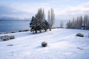a snow covered field with trees and a body of water at Blue Aparts Dina Huapi Bariloche in Dina Huapi +26 photos