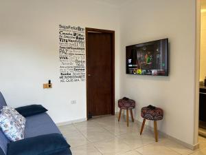 a living room with a couch and a tv and two stools at BORA BORA Hospedagens in Joinville
