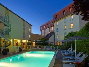 a pool in front of a building with chairs and umbrellas at ibis Beaune Centre in Beaune