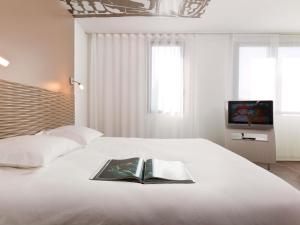 a bedroom with a white bed with a book on it at ibis Styles Lille Aéroport in Lesquin