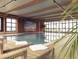 a swimming pool with two chairs in a building at Mercure Hotel am Messeplatz Offenburg in Offenburg