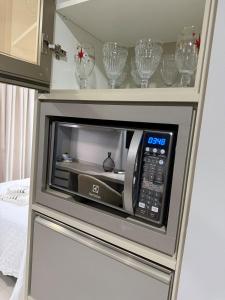 a microwave oven in a cabinet with wine glasses at Studio Premium - Bairro Nova Yorque Araçatuba in Araçatuba