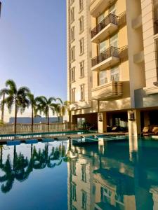 a swimming pool in front of a building with palm trees at Saint Honore Executive 1 Full bed, 1 Sofa bed 1 Pull out bed 2BR in Iloilo City