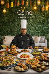 a man in a chefs hat sitting at a table full of food at The saffron anandamvillas in Kurukshetra