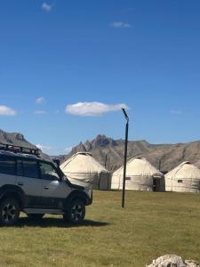 a suv parked in front of a field with tents at NOMAD KEL-SUU Yurt Camp in Kol-Suu