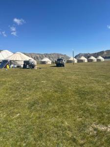 a field of grass with tents in the background at NOMAD KEL-SUU Yurt Camp in Kol-Suu +18 photos