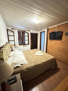 a bedroom with a bed and a tv on a brick wall at Pousada do Sino - 2 min do Capivari in Campos do Jordão