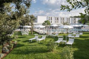 a row of white chairs and umbrellas on the lawn of a hotel at Hotel Park Punat managed by Falkensteiner in Punat