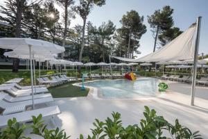 a pool with white chairs and umbrellas at Hotel Park Punat managed by Falkensteiner in Punat +23 photos
