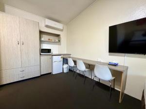 a room with a table with white chairs and a flat screen tv at Ashwood Motel in Gosford