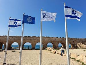 four blue and white flags on the beach at The Caesar Stay in Caesarea +5 photos
