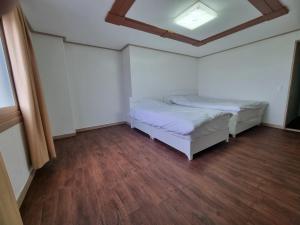 two beds in a room with wood floors and a ceiling at Orasung Motel in Jeju