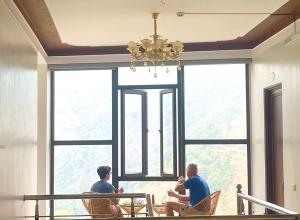 two men sitting in chairs in front of a large window at Nhà Nghỉ Mũi Giày in Mù Cang Chải