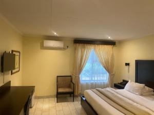 a bedroom with a bed and a window with a chair at Villa Via Hotel Midrand in Midrand