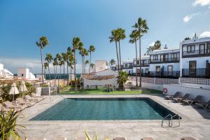a swimming pool in front of a building with palm trees at Makāi Bungalows in Playa del Aguila